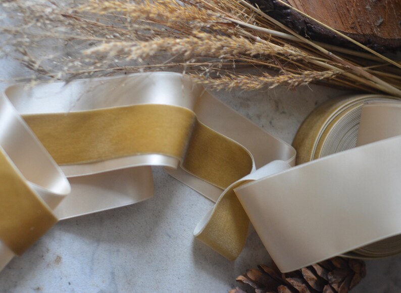 May include: A roll of ivory satin ribbon with a gold velvet trim. The ribbon is folded and arranged on a white surface.