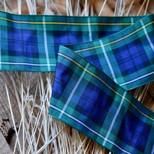 May include: Blue, green, and white plaid ribbon with a yellow stripe. The ribbon is folded and lying on a wooden surface.