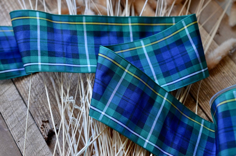May include: Blue, green, and white plaid ribbon with a yellow stripe. The ribbon is folded and lying on a wooden surface.