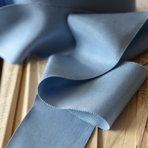 May include: A close-up of a light blue grosgrain ribbon folded on a stack of old books. The ribbon has a subtle ribbed texture.