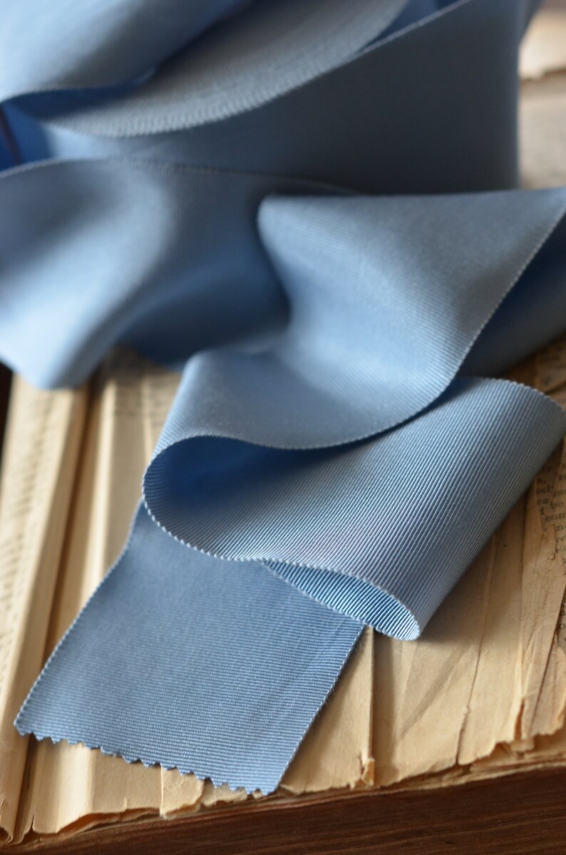 May include: A close-up of a light blue grosgrain ribbon folded on a stack of old books. The ribbon has a subtle ribbed texture.