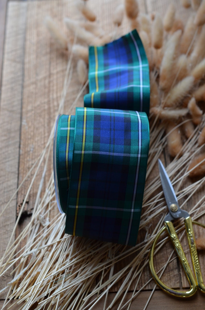 May include: A roll of green, blue, and yellow plaid ribbon with a pair of gold scissors on a wooden surface.