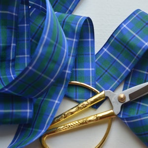 May include: Blue and green plaid ribbon with gold-colored scissors. The ribbon is folded and the scissors are placed on top of it.