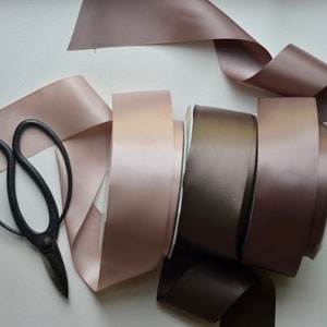 May include: A collection of brown satin ribbon spools with a pair of black scissors. The ribbon is arranged in a circular pattern, with the scissors placed on top.