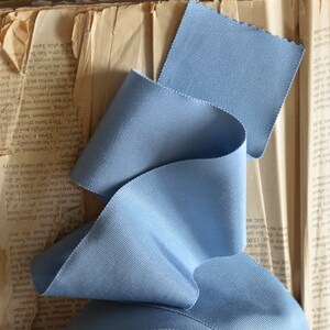 May include: A roll of light blue grosgrain ribbon with a textured surface. The ribbon is folded and arranged on top of a vintage book.