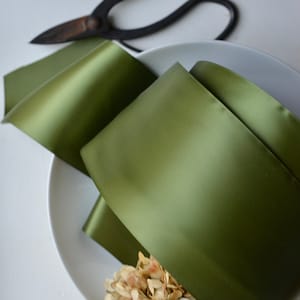 May include: A roll of olive green satin ribbon on a white plate with dried hydrangeas.