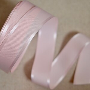 May include: A pale pink satin ribbon with a textured, ribbed surface. The ribbon is curled and folded, showing the sheen of the satin.