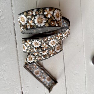 May include: A roll of black and gold floral trim with white flowers. The trim is made of a soft, woven fabric and has a delicate, embroidered design.