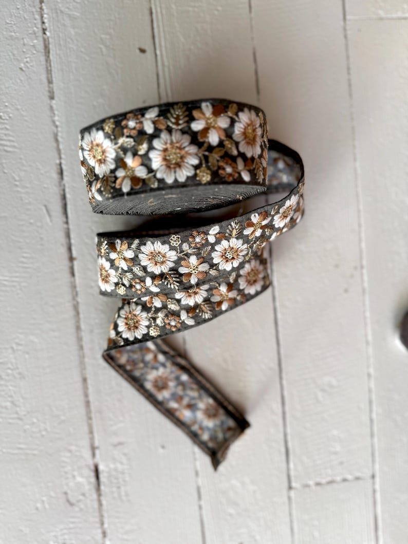 May include: A roll of black and gold floral trim with white flowers. The trim is made of a soft, woven fabric and has a delicate, embroidered design.