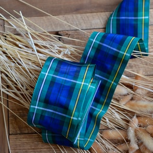May include: A blue, green, white, and yellow plaid ribbon with a satin finish. The ribbon is lying on a wooden surface with dried grass.