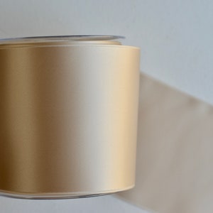 May include: A spool of beige satin ribbon wrapped in clear plastic.