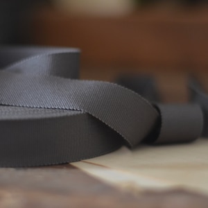May include: A close-up of a gray woven ribbon, rolled up and ready for crafting projects.