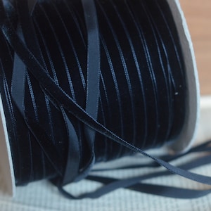 May include: A spool of black velvet ribbon. The ribbon is wound around a white cardboard spool.