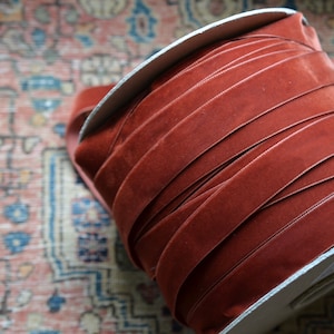 Könnte beinhalten: Eine Spule mit rostfarbenem Samtband. Das Band ist fest um einen Pappkern gewickelt.