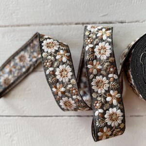 May include: A close-up of a black and white floral trim ribbon with gold accents. The ribbon is folded and twisted, showing the intricate details of the embroidery.