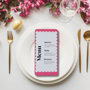 Może przedstawiać: Różowa karta menu z białym falistym obramowaniem i słowem "Menu" w pogrubionych czarnych literach. Menu zawiera przystawkę, danie główne i deser. Karta leży na białym talerzu ze złotym widelcem i nożem.