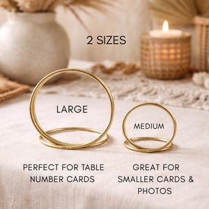 Puede incluir: Dos portatarjetas redondos de metal dorado, uno grande y otro mediano, para números de mesa y tarjetas o fotos más pequeñas. El texto "2 SIZES" está en la parte superior. El portatarjetas grande está etiquetado como "LARGE" y el mediano como "MEDIUM".