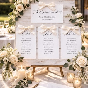May include: A rustic wooden wedding seating chart with cream-colored bows and floral arrangements. The chart displays guest names under the headings "One," "Two," and "Three," with the text "Find your seat!" at the top. The date is September 25th, 2027.
