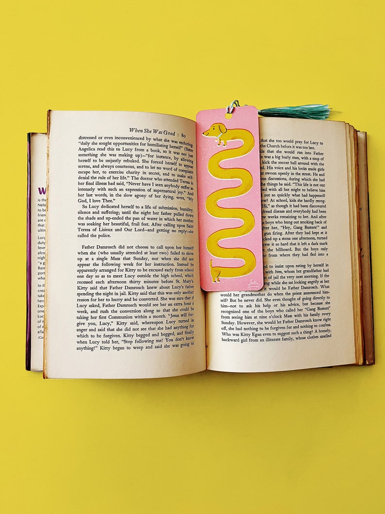 May include: A pink and yellow bookmark with a cartoon dachshund illustration. The bookmark features the text "When She Was Good: Bo" and a quote from the book.