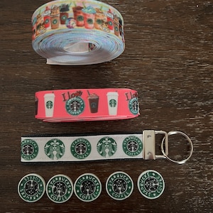 Peut inclure: Un ensemble de ruban, porte-clés et boutons sur le thème de Starbucks. Le ruban est rose avec des gobelets Starbucks blancs et noirs et le texte "J'aime Starbucks Coffee". Le porte-clés est noir avec des logos Starbucks blancs et verts. Les boutons sont verts avec des logos Starbucks blancs.