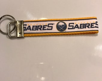 May include: A yellow and white key chain with the Buffalo Sabres logo and the text "Buffalo Sabres" printed on it.
