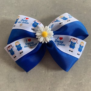 May include: Blue and white ribbon bow with a white daisy flower accent. The ribbon has a repeated pattern of a girl scout in uniform with the text "I love Daisy Girl Scouts".