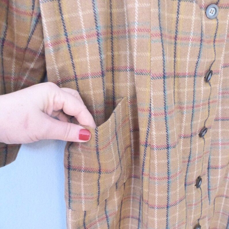 May include: A brown plaid shirt with a patch pocket on the left side. The shirt has a button-up front and a collar.
