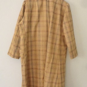 May include: A long-sleeved, brown and tan plaid coat with a collared neckline. The coat is hanging on a white hanger.