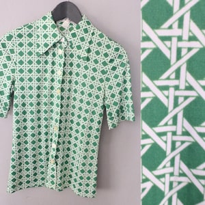 May include: A green and white short-sleeved button-up shirt with a geometric pattern. The pattern is a woven design of white lines on a green background.