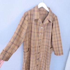 May include: A long-sleeved brown and tan plaid shirt dress with a collared neckline and button closure. The dress has two patch pockets on the front.