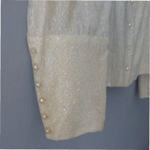 Puede incluir: Primer plano de una tela blanca brillante con botones de perla a lo largo del lado de la manga.