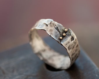 May include: A silver ring with a textured finish and three small gold dots. The ring is wide and has a unique, organic shape.