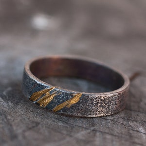 Op de afbeelding: Een zilveren ring met een getextureerde afwerking en dunne gouden strepen.