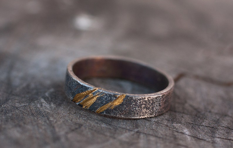 Op de afbeelding: Een zilveren ring met een getextureerde afwerking en dunne gouden strepen.