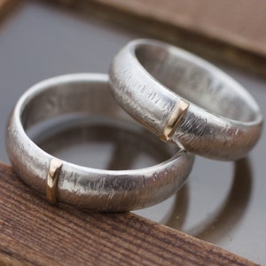 May include: Two silver wedding bands with a textured finish and a thin gold band inset into each ring.