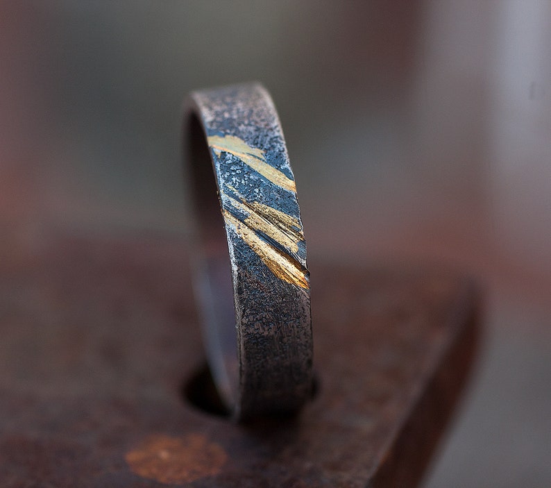 Op de afbeelding: Een zilveren ring met een textuur en gouden accenten. De ring is een eenvoudige band met een diagonaal patroon van gouden lijnen.