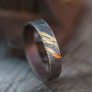 Op de afbeelding: Een zilveren ring met een getextureerde afwerking en gouden accenten. De gouden accenten zijn in een diagonaal patroon.