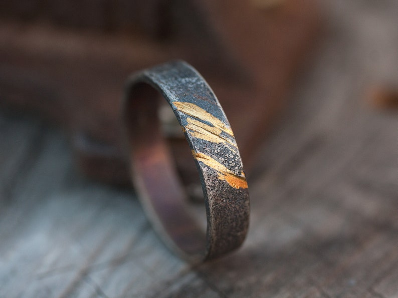 Op de afbeelding: Een zilveren ring met een getextureerde afwerking en gouden accenten. De gouden accenten zijn in een diagonaal patroon.