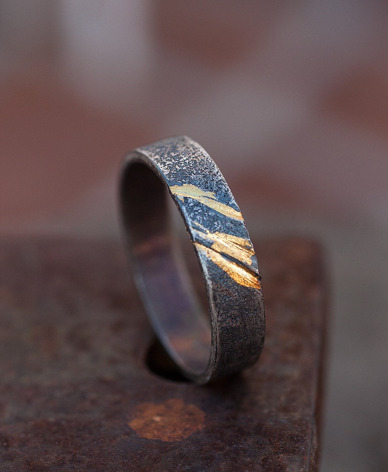 Op de afbeelding: Een zilveren ring met een getextureerde afwerking en dunne gouden strepen.