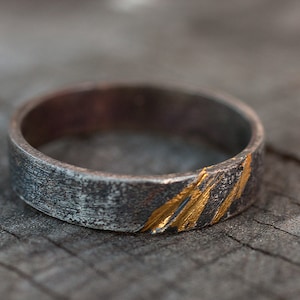Op de afbeelding: Een zilveren ring met een getextureerde afwerking en gouden accenten. De ring heeft een brede band en een eenvoudig ontwerp.
