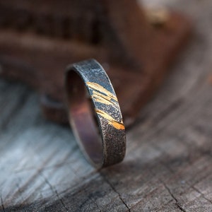 Op de afbeelding: Een zilveren ring met een dunne band en een gouden inlay-ontwerp. De ring ligt op een houten oppervlak.