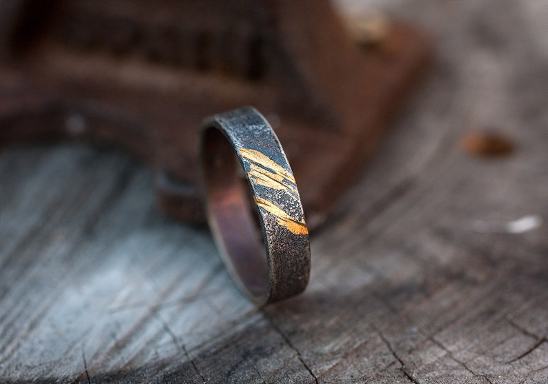 Op de afbeelding: Een zilveren ring met een dunne band en een gouden inlay-ontwerp. De ring ligt op een houten oppervlak.