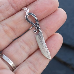 May include: A silver knife pendant necklace with a twisted handle and a textured blade.