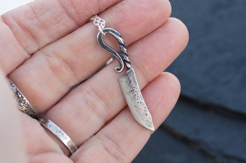 May include: A silver knife pendant necklace with a twisted handle and a textured blade.
