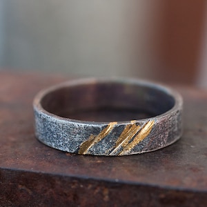 Op de afbeelding: Een zilveren ring met een getextureerde afwerking en dunne gouden strepen.