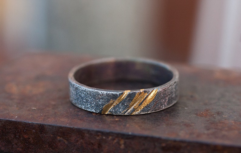 Op de afbeelding: Een zilveren ring met een getextureerde afwerking en dunne gouden strepen.