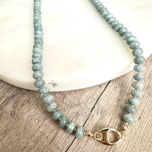 May include: A beaded necklace featuring pale green beads with a gold-colored clasp. The beads are evenly sized and strung together, creating a smooth, rounded shape. The clasp is a decorative element, adding a touch of elegance to the necklace.