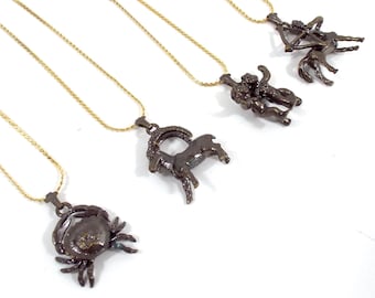 May include: Four gold chain necklaces with different zodiac sign pendants. The pendants are made of dark metal and feature the signs of Sagittarius, Gemini, Capricorn, and Cancer.