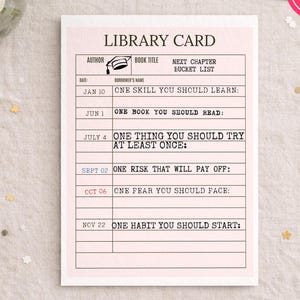 May include: A pink and white library card with the text "LIBRARY CARD" at the top. The card includes prompts for a bucket list, such as "ONE SKILL YOU SHOULD LEARN" and "ONE BOOK YOU SHOULD READ". The words "INSTANT DOWNLOAD" are in a pink circle.