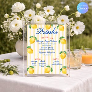 May include: A clear acrylic drinks menu with a yellow and white striped background, adorned with lemon illustrations. The menu lists cocktails, beer, and wine options. The word "Drinks" is written in elegant blue script.